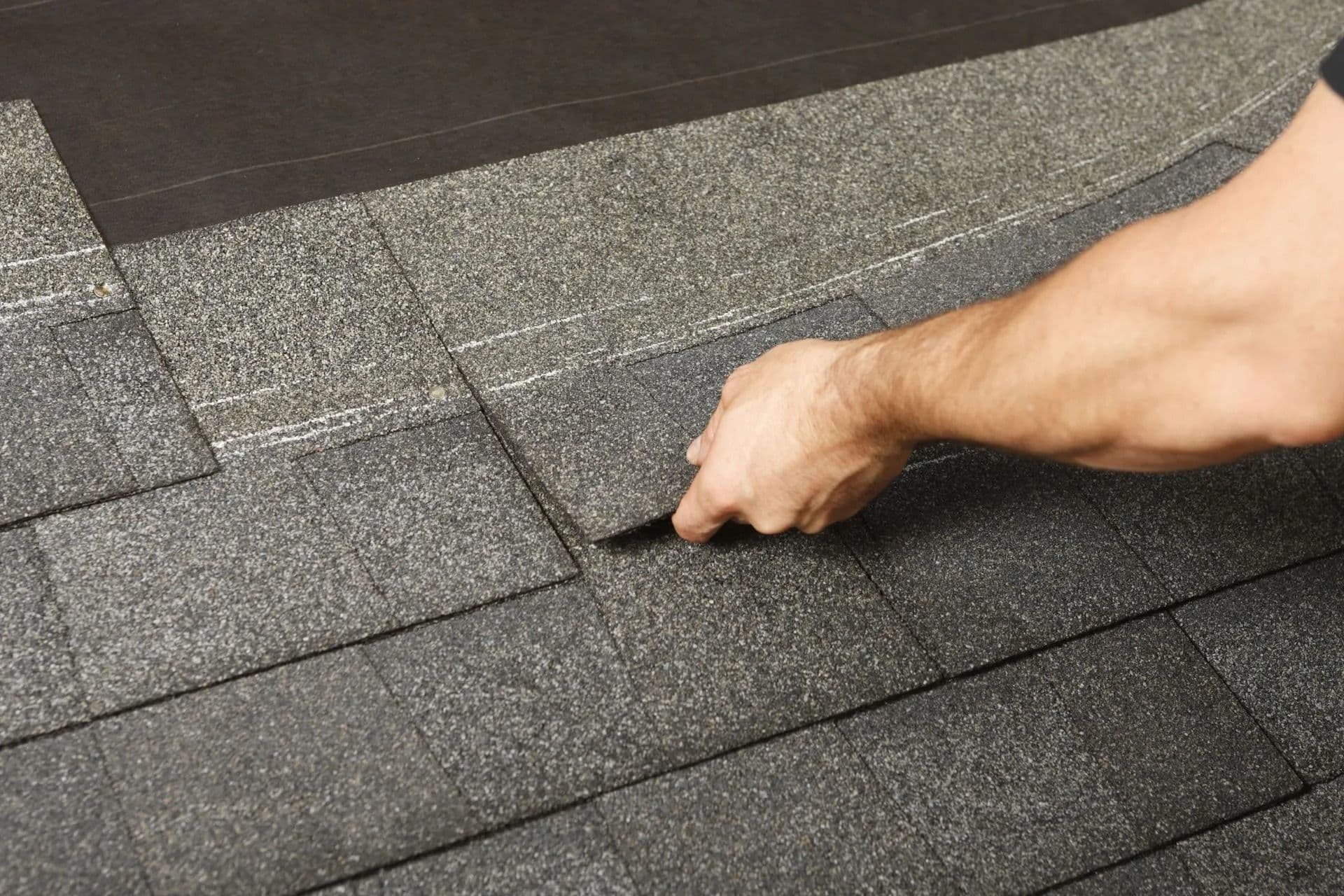 A person's hand skillfully installs dark gray asphalt shingles on a roof, illustrating careful craftsmanship in home construction and repair.