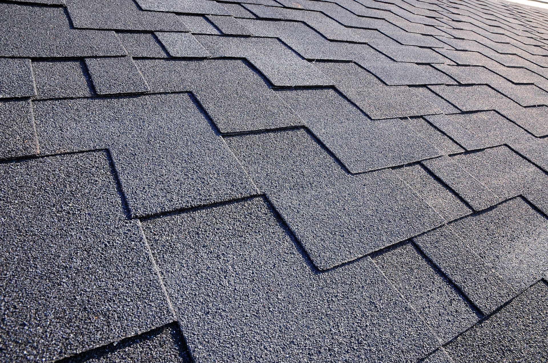 Close-up of a textured gray roof with overlapping asphalt shingles in a zigzag pattern, conveying durability and weather resistance.